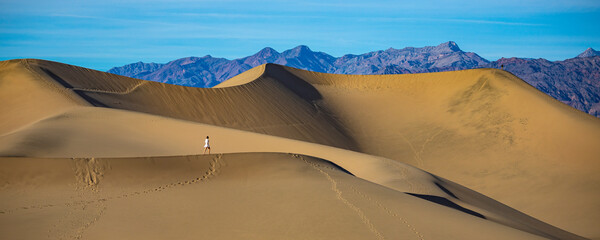 Fototapeta na wymiar girl in white dress lost in the desert; walking on large sand dunes in mesquite flat sand dunes in death valley national park, california, usa