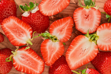 Ripe strawberries and berry halves on a wooden table, seasonal berry harvest, top view, idea for strawberry background or dessert preparation