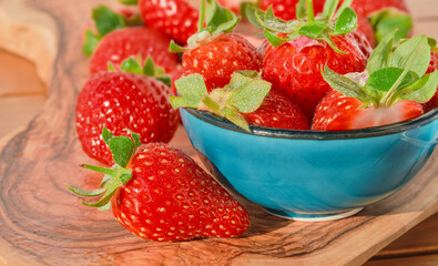 Fresh strawberries with water drops in a blue bowl on a wooden table natural sunlight, selective focus, strawberry spring season