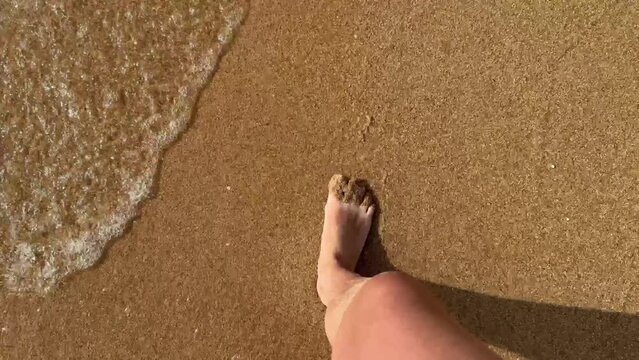 SLOW MOTION Watching your bare feet as you walk along a yellow sand beach lapped by crystal clear ocean water. First person view of a man on vacation walking on a tropical sandy beach. High quality 4k