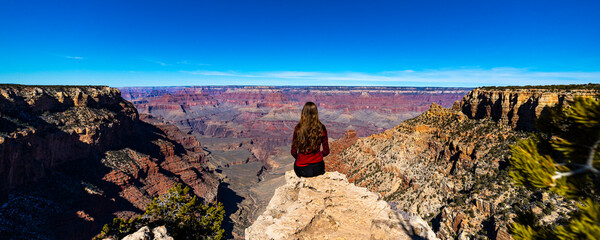 long haired hiker girl sitting on the edge of grand canyon; hiking in the grand canyon national park during spring, spring panorama of grand canyon