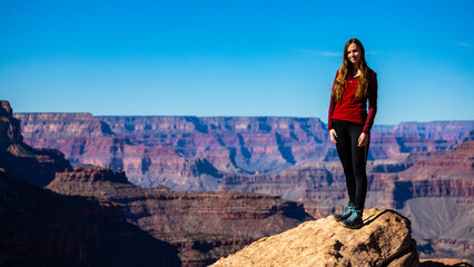 Naklejka premium Beautiful long-haired smiling tourist girl stands with her back to the Grand Canyon. Traveling in winter in Grand Canyon National Park, Arizona, USA.