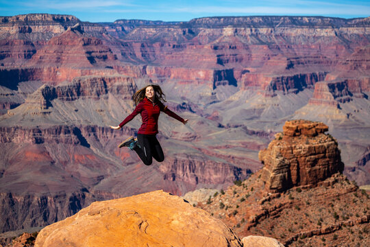 long haired hiker girl jumping for joy in front of great canyon; hiking in great canyon national park during spring; flying above great canyon in arizona
