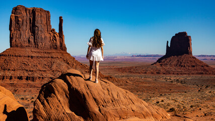 Beautiful long haired girl in white dress admires mighty unique famous rock formations in Monument Valley Navajo Tribal Park, Utah; Arizona, USA
