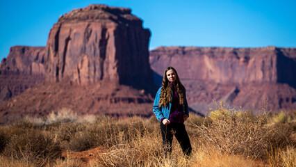Naklejka premium girl in denim jacket walks through monument valley with massive monuments in the background; walk in the wild west, scene from a western