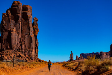 girl in denim jacket walks through monument valley with massive monuments in the background; walk...
