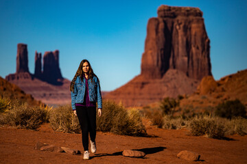 girl in denim jacket walks through monument valley with massive monuments in the background; walk in the wild west, scene from a western