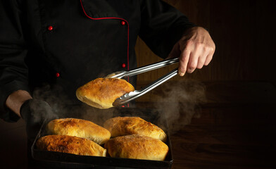 The baker bakes hot dog buns. Tongs in chef hand and baking sheet with hot pies. Place for recipe or menu