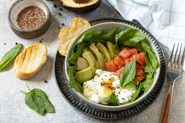 Classic breakfast, brunch - with poached egg, avocado, arugula, flax seeds and salted salmon on a gray background.