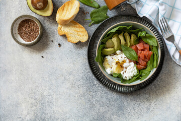 Classic breakfast, brunch - with poached egg, avocado, arugula, flax seeds and salted salmon on a gray background. View from above. Copy space.