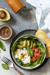 Classic breakfast, brunch - with poached egg, avocado, arugula, flax seeds and salted salmon on a gray background. View from above. Copy space.