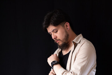 Fototapeta na wymiar Medium close up shot of a young white man with a beard looking at his wrist watch on a black background