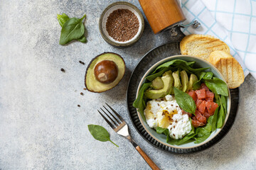 Classic breakfast, brunch - with poached egg, avocado, arugula, flax seeds and salted salmon on a gray background. View from above. Copy space.