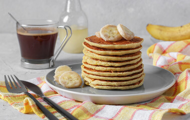 Banana cornmeal pancakes, a slide on a plate, and cup of coffee and banana syrup to serve