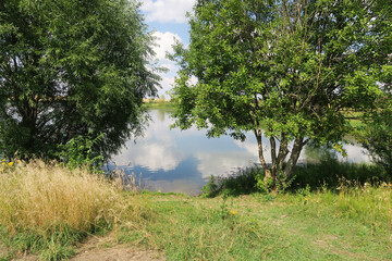 Reflection of the sky with clouds on the shore of a large lake on a sunny summer day.