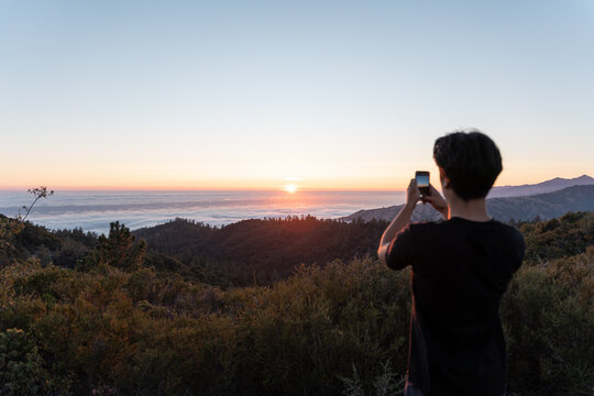 A young man is taking a photo of the sunset landscape with his phone