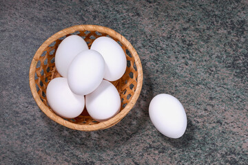 several fresh chicken eggs in a straw basket on a wooden background. Healthy eating concept.