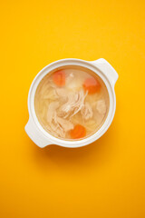 bowl of chicken broth with chicken and carrot in yellow