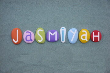 Jasmiyah, female given name composed with multi colored stone letters over green sand