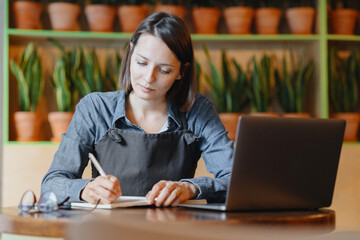 female manager of restaurant works on a laptop, makes note in notebook reserve, manages finances of coffee shop. business woman owned chain of fast food takeaways. small business