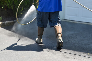 Lower body of a handyman wearing shorts spraying water to pressure wash a driveway - obrazy, fototapety, plakaty