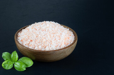 Himalayan crystalline pink salt in a wooden bowl on a black background. 