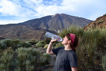 Fototapeta na wymiar Pretty young traveler woman hiking drinking water on mountain with Teide volcano on the background. Enjoying hot weather and sun in Spain. Staying hydrated on sport hike. Break for water on trip walk