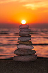 Vertical İmage, Balanced pebble pyramid silhouette on the beach on sunset. Sea on the background. Zen stones on the sea beach, meditation, spa, harmony, calmness, balance concept.