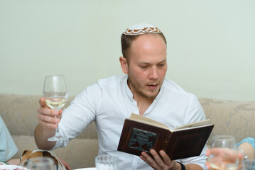 Young bearded man with wine in the glass reading Haggadah. Jewish family celebrating Passover at the table with traditional food. Family Passover dinner seder.