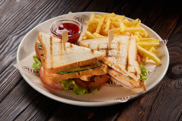 Two sandwiches with french fries and ketchup on white plate on wooden table