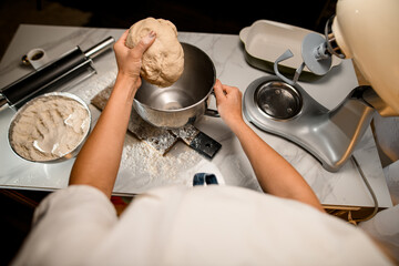 female hands holding bread dough over stainless bowl on table