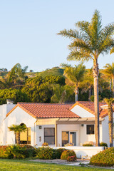 Beautiful houses with nicely landscaped front the yard, and green hills in the background in a small beach town in California at sunset
