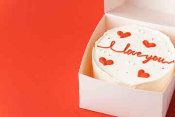 Korean style bento cake in a white gift box on the red festive background. Little cake with I love you inscription. Happy Valentine's Day