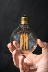 Close-up of man hand holding incandescent lamp with tungsten filament glowing. Saving energy and...