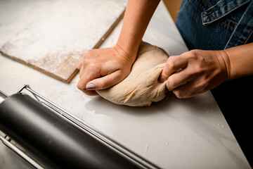 Top view on female hands kneading raw bread dough on wooden board.