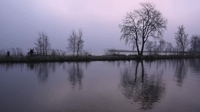 silhouette of a pair of cyclists and trees on a cyclepath fietspad in the rural wetland area of Reeuwijk in early winter morning sunrise where people live with nature around beautiful lakes