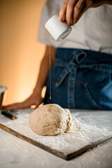 dough on cutting board with flour and female hand pours oil from a cup onto it.