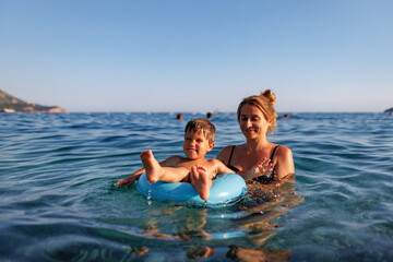 Fototapeta na wymiar Caring mother rides her son on an inflatable ring in the sea