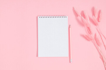 Empty notepad mockup, dry flowers, fluffy rabbit tail flower on pink background. Spiral open...