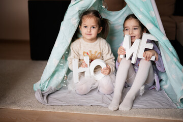 Two girls sisters at wigwam tent with wooden home letters. © AS Photo Family