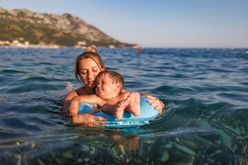 Fototapeta premium Caring mother rides her son on an inflatable ring in the sea