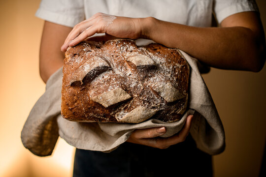 Close-up view of delicious freshly baked rustic organic loaf of bread in hands of woman.