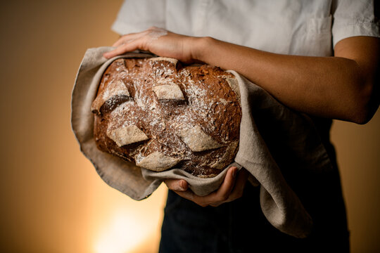 delicious freshly baked rustic organic loaf of bread in hands of woman.