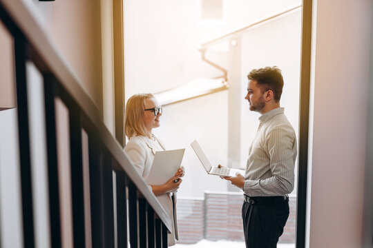 Two Business People Man And Woman Are Standing Opposite Each Other In A Large Corridor And Talking. Concept Of Successful Business.