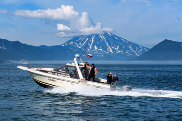 A boat with tourists floats in the Pacific Ocean against the backdrop of a snow-covered volcano and...