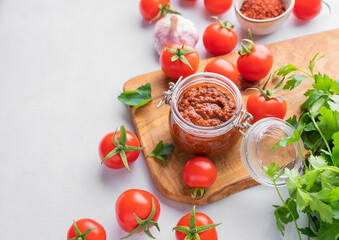 Fototapeta na wymiar Salsa or adjika sauce is a traditional Mexican or Caucasus sauce with tomatoes and hot peppers on a light background with fresh herbs.