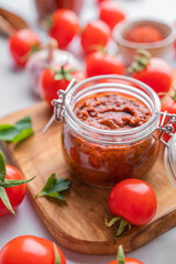 Salsa or adjika sauce is a traditional Mexican or Caucasus sauce with tomatoes and hot peppers on a light background with fresh herbs close up. Concept of a vegetarian food.