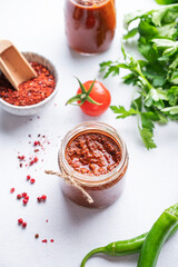 Hot sauce adjika. Homemade appetizer with pepper and tomatoes in a jar on light background with fresh herb and vegetables. Top view.