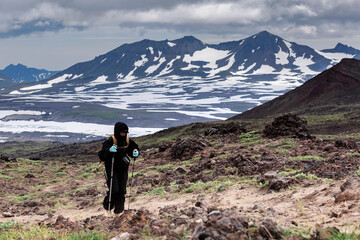 A girl walks along a volcano, lava frozen against the backdrop of a volcano and mountains, clouds, Kamchatka.