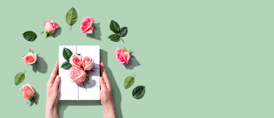 Female hands holding a gift box with pink roses overhead view - flat lay
